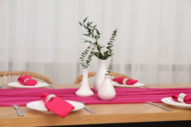 Beautiful table setting and vases with green branches in dining room