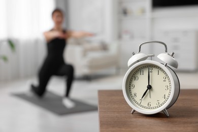 Photo of Morning routine. Alarm clock on wooden table and woman doing exercise, selective focus. Space for text