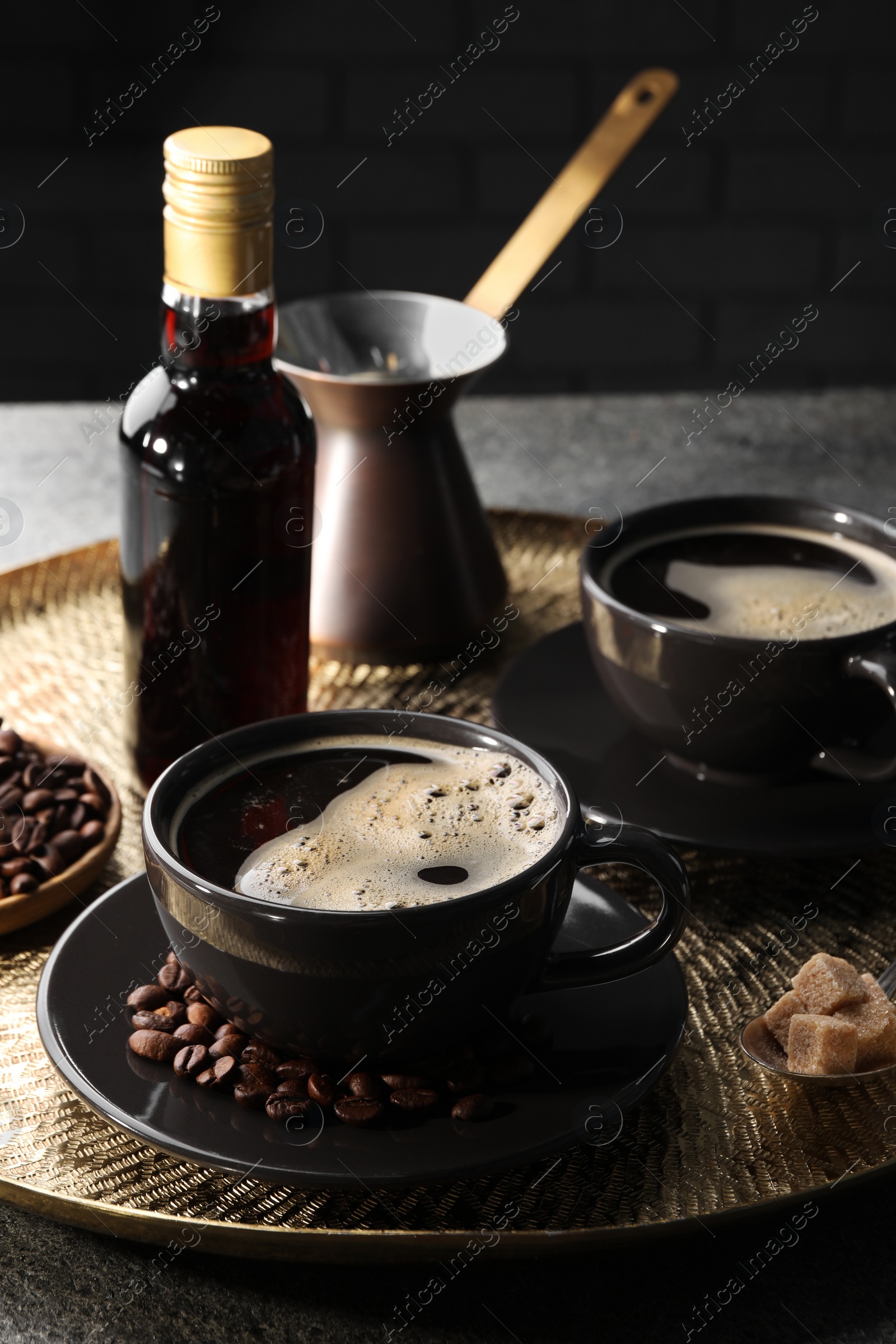 Photo of Bottle of delicious syrup, beans and cups of coffee on grey table