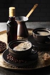 Bottle of delicious syrup, beans and cups of coffee on grey table