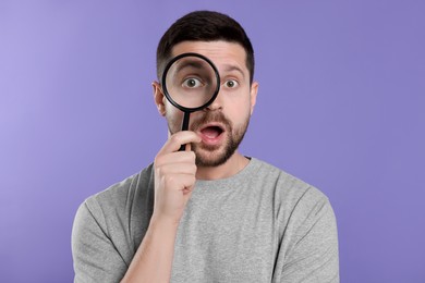 Photo of Surprised man looking through magnifier glass on violet background