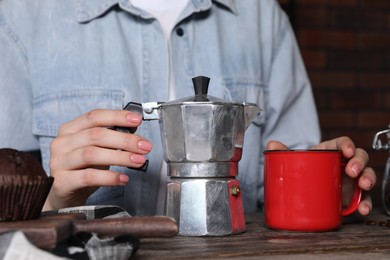 Photo of Brewing coffee. Woman with moka pot, cup and muffin at wooden table, closeup