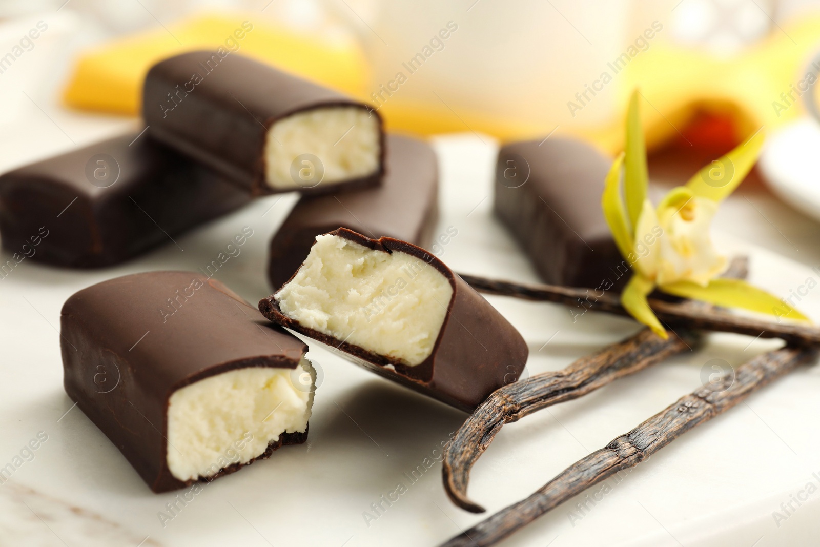 Photo of Glazed curd cheese bars, vanilla pods and flower on white board, closeup