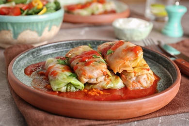 Photo of Plate with stuffed cabbage leaves in tomato sauce on table