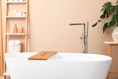 Photo of Bath tub with wooden board and different personal care products and accessories on shelving unit in bathroom