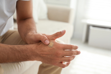 Photo of Man putting sticking plaster onto hand indoors, closeup