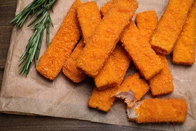 Photo of Fresh breaded fish fingers with rosemary served on wooden table, top view