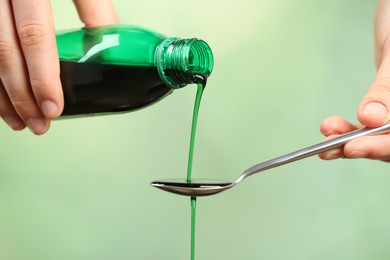 Woman pouring cough syrup into spoon on light green background, closeup