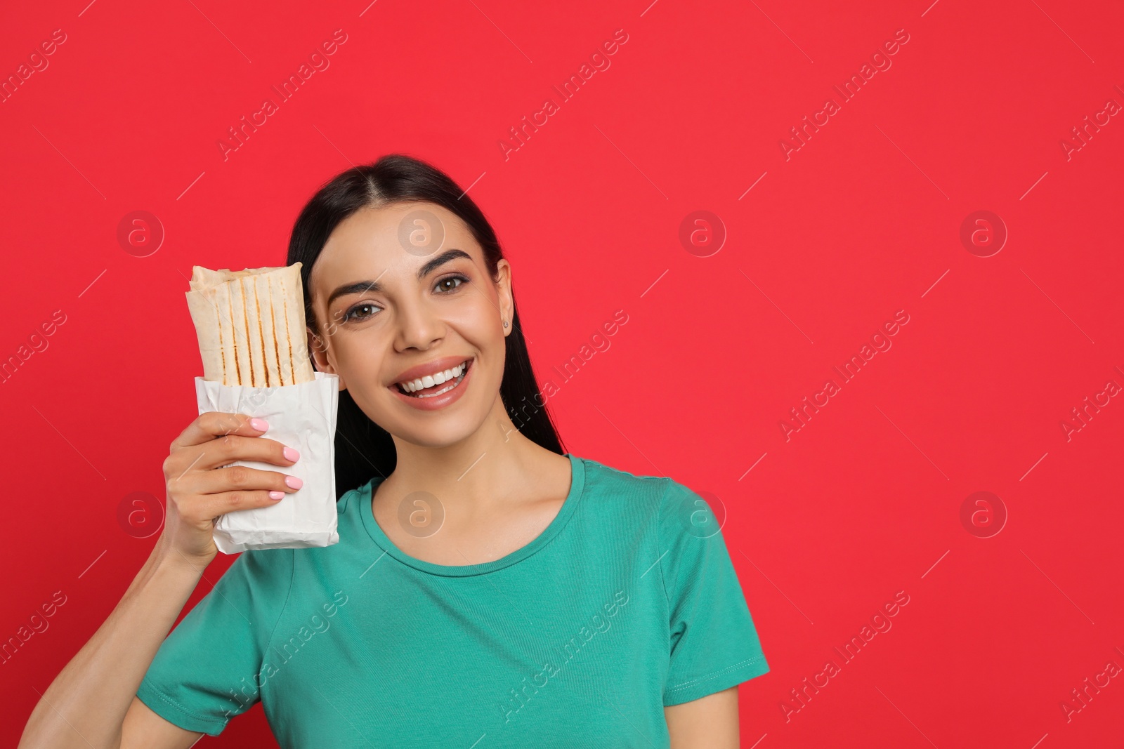 Photo of Happy young woman with delicious shawarma on red background