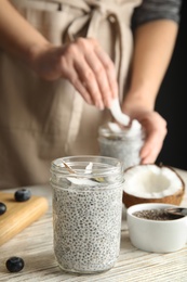 Jar of tasty chia seed pudding with coconut on table against blurred background