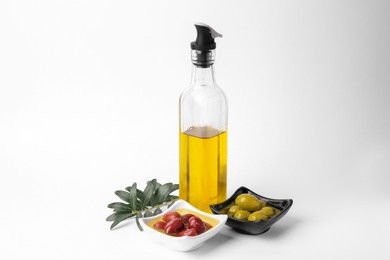 Bottle of cooking oil, olives and leaves on white background