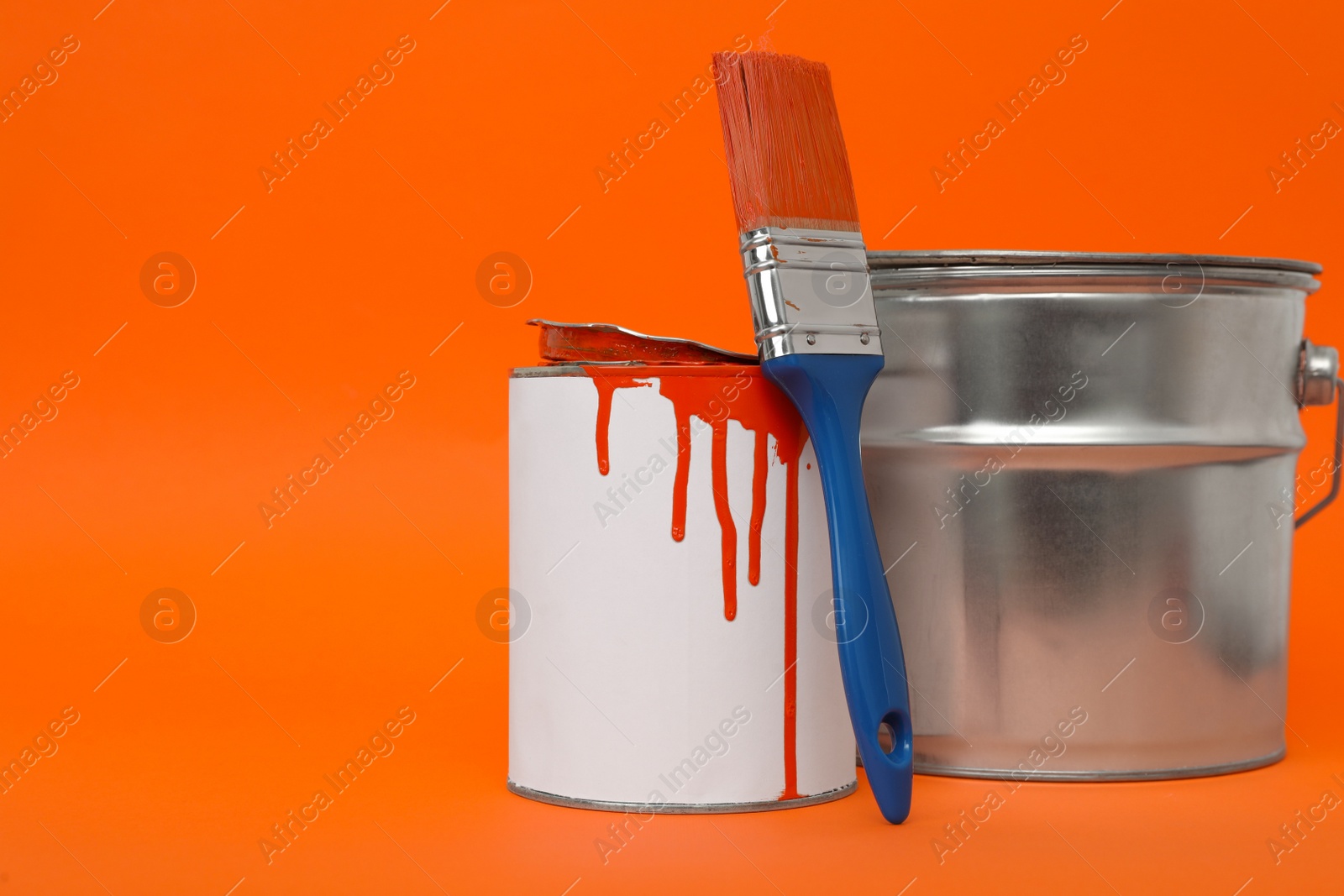 Photo of Cans of orange paint and brush on color background. Space for text