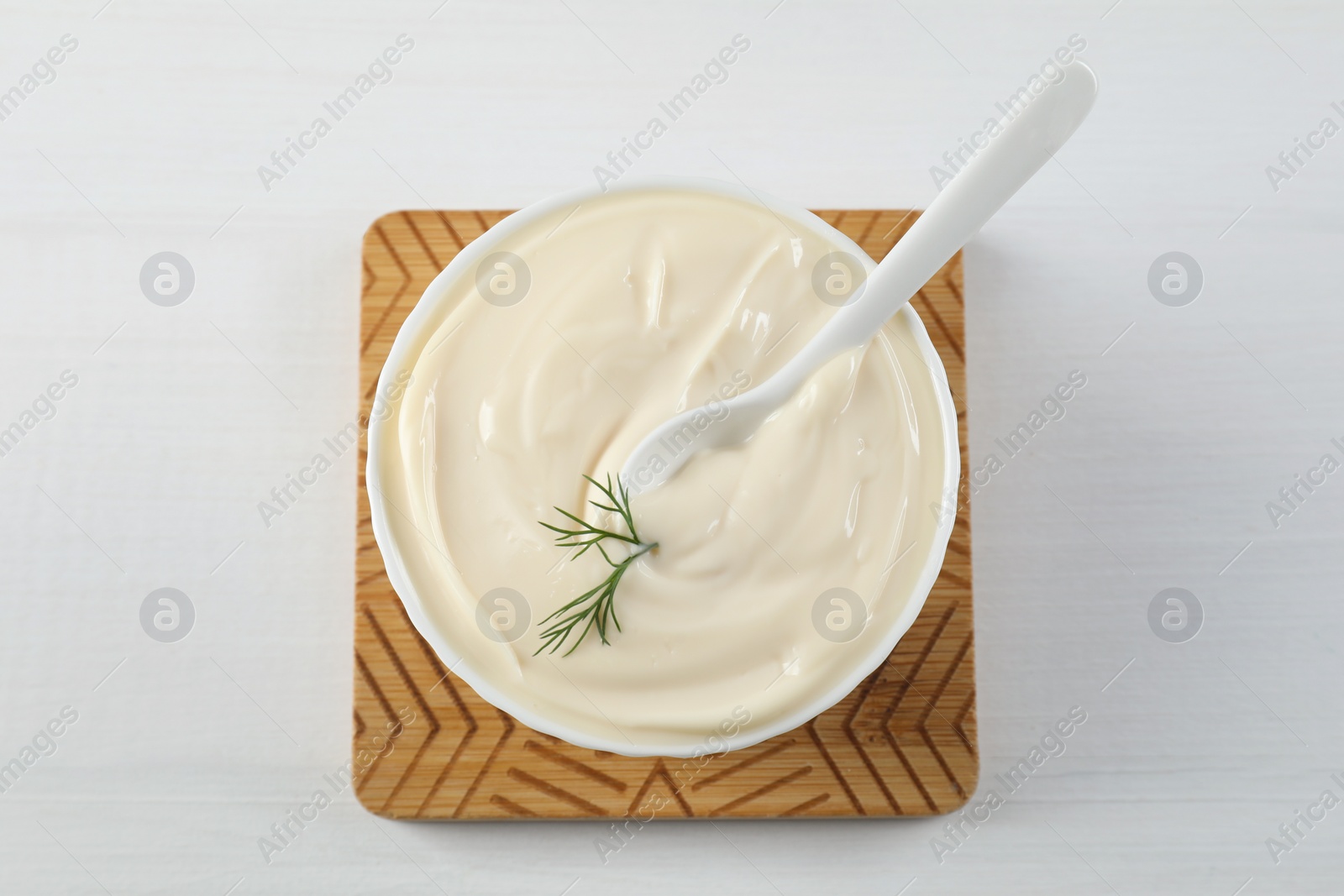 Photo of Fresh mayonnaise sauce in bowl on white wooden table, top view