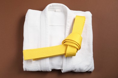 Photo of Yellow karate belt and white kimono on brown background, top view