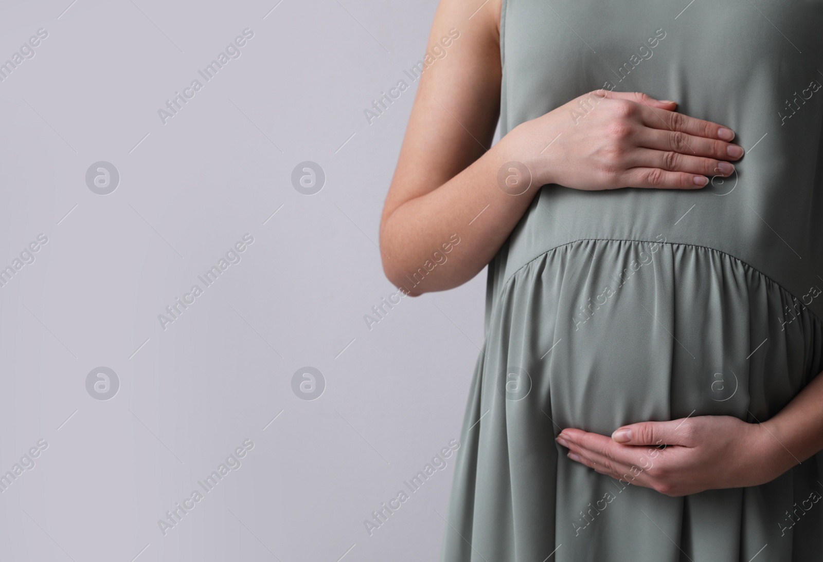 Photo of Pregnant woman on light grey background, closeup. Space for text