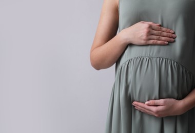 Pregnant woman on light grey background, closeup. Space for text