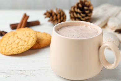 Photo of Delicious hot cocoa drink in cup and cookies on white wooden table, closeup