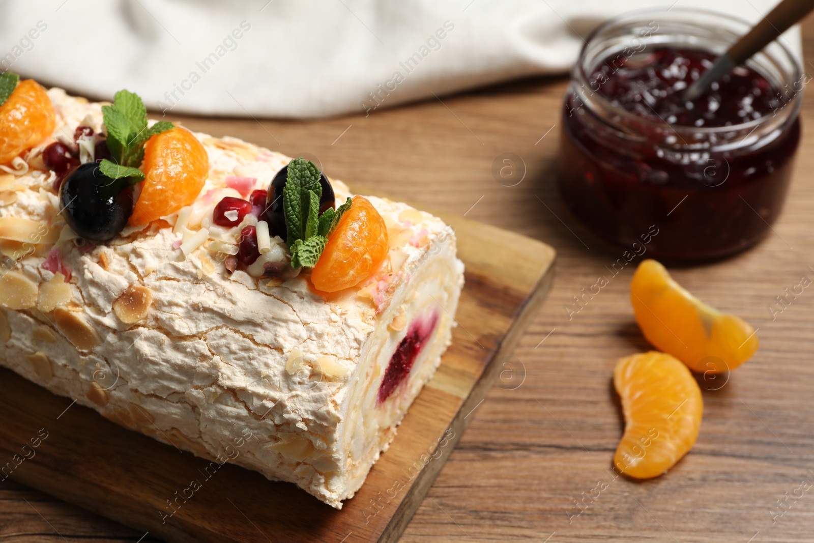 Photo of Tasty meringue roll with jam, tangerine slices and mint leaves on wooden table, closeup