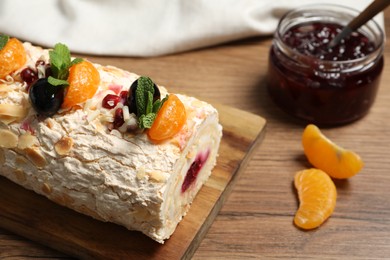 Tasty meringue roll with jam, tangerine slices and mint leaves on wooden table, closeup