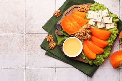 Delicious persimmon, blue cheese, nuts and honey served on tiled surface, flat lay. Space for text