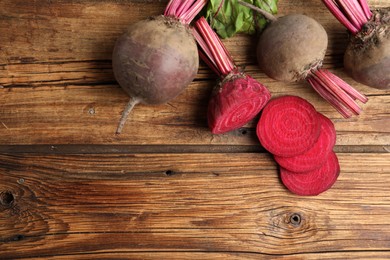 Photo of Cut and whole raw beets on wooden table, flat lay. Space for text