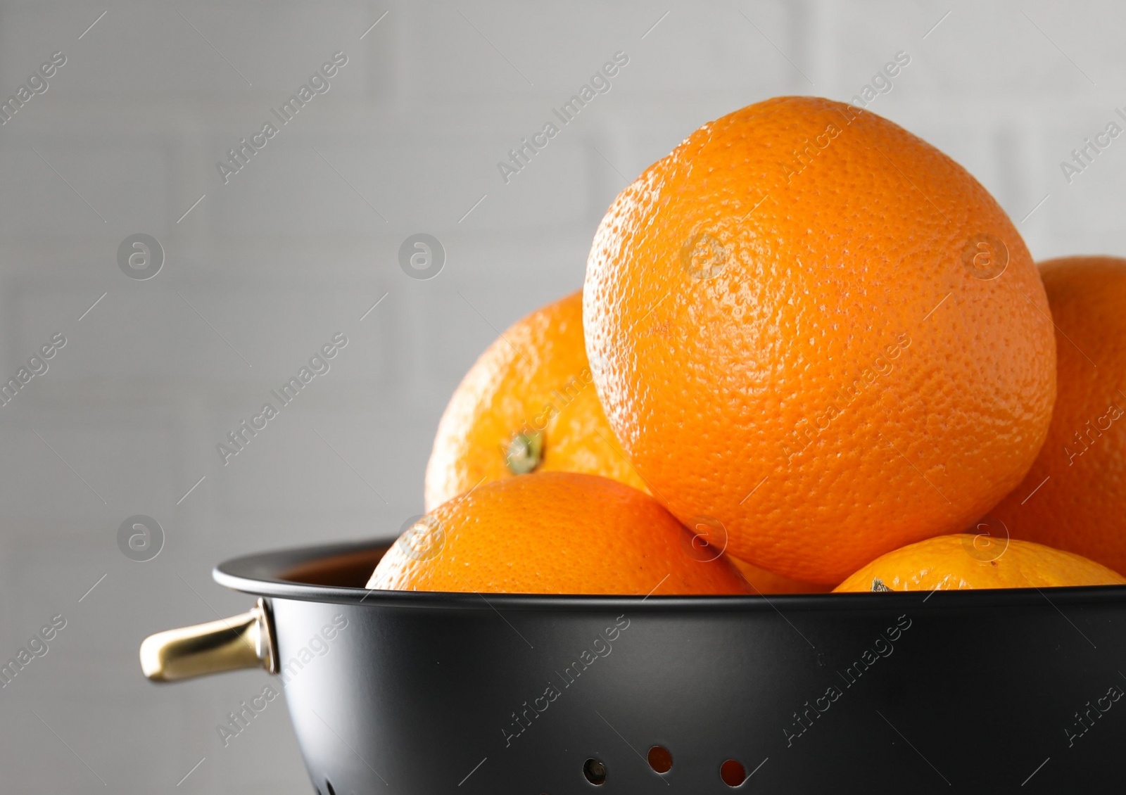 Photo of Fresh ripe oranges in black colander on light background, closeup. Space for text