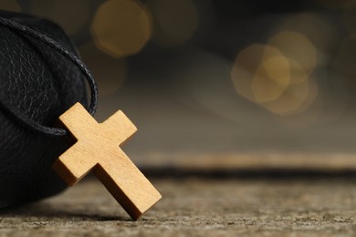 Photo of Christian cross on wooden table against blurred background, closeup. Space for text