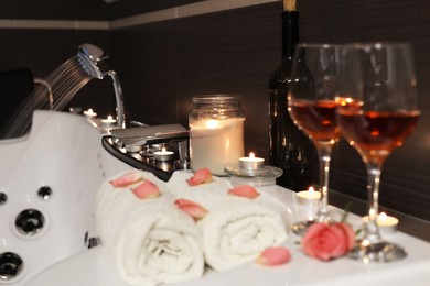 Photo of Glasses of wine, towels and rose on tub in bathroom. Romantic atmosphere