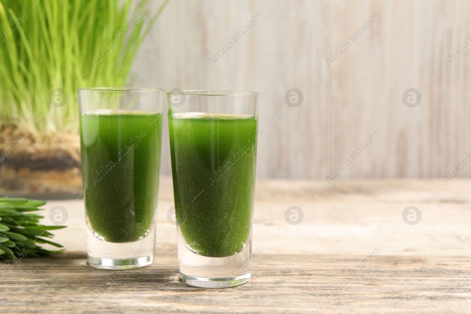 Photo of Wheat grass drink in shot glasses on wooden table, closeup. Space for text