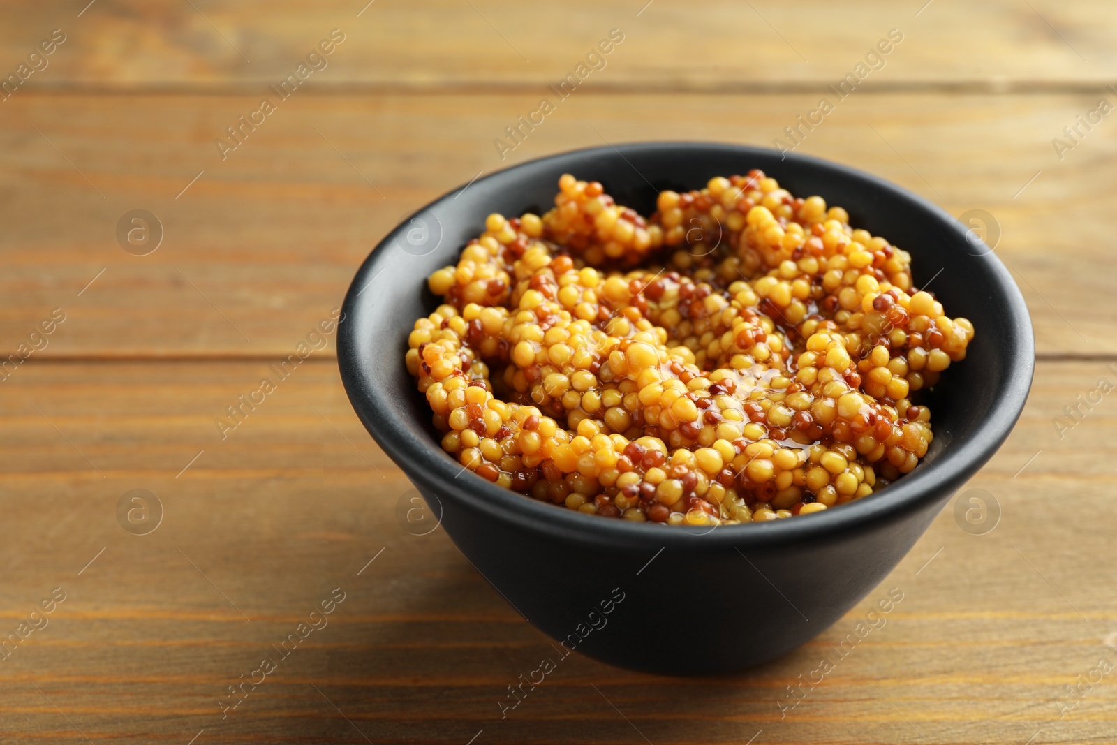 Photo of Fresh whole grain mustard in bowl on wooden table, closeup. Space for text