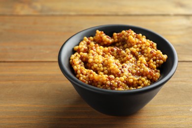 Photo of Fresh whole grain mustard in bowl on wooden table, closeup. Space for text