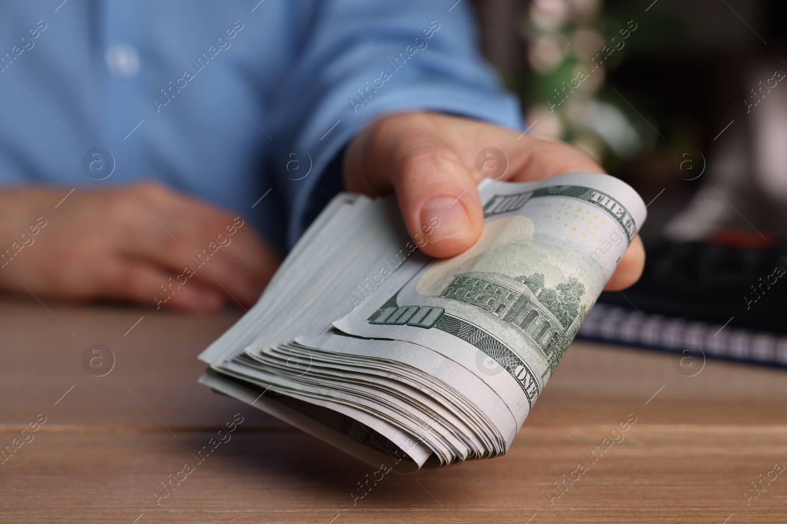 Photo of Money exchange. Woman holding dollar banknotes at wooden table, closeup