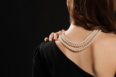 Photo of Young woman wearing elegant pearl necklace on black background, closeup. Space for text