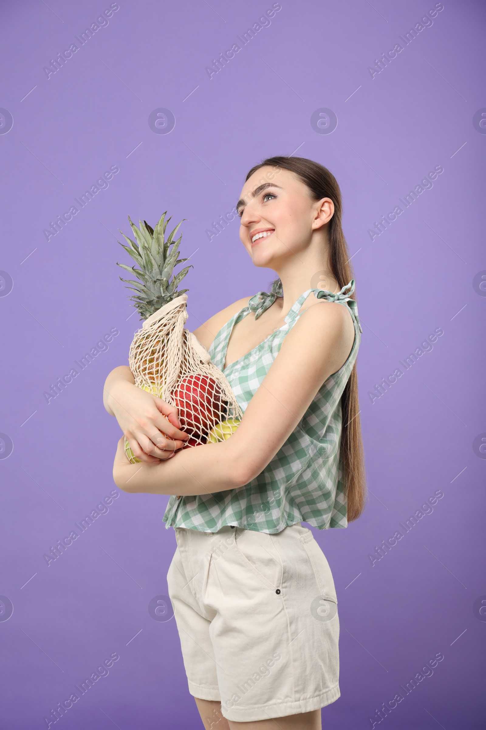 Photo of Woman with string bag of fresh fruits on violet background