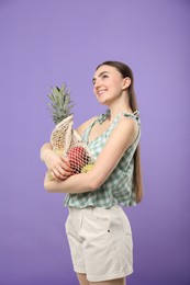 Woman with string bag of fresh fruits on violet background