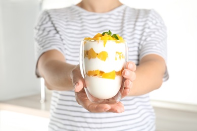 Woman holding glass of tasty peach dessert with yogurt in kitchen, closeup