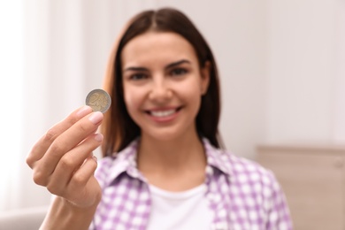 Photo of Happy young woman holding coin at home, focus on hand