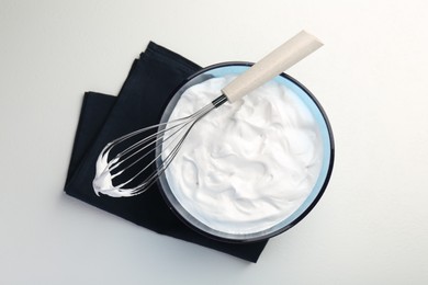 Bowl with whipped cream and whisk on light background, top view