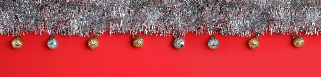 Image of Silver tinsel and Christmas balls on red background, flat lay. Banner design