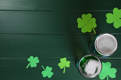 Photo of St. Patrick's day party. Green beer and decorative clover leaves on wooden table, flat lay. Space for text
