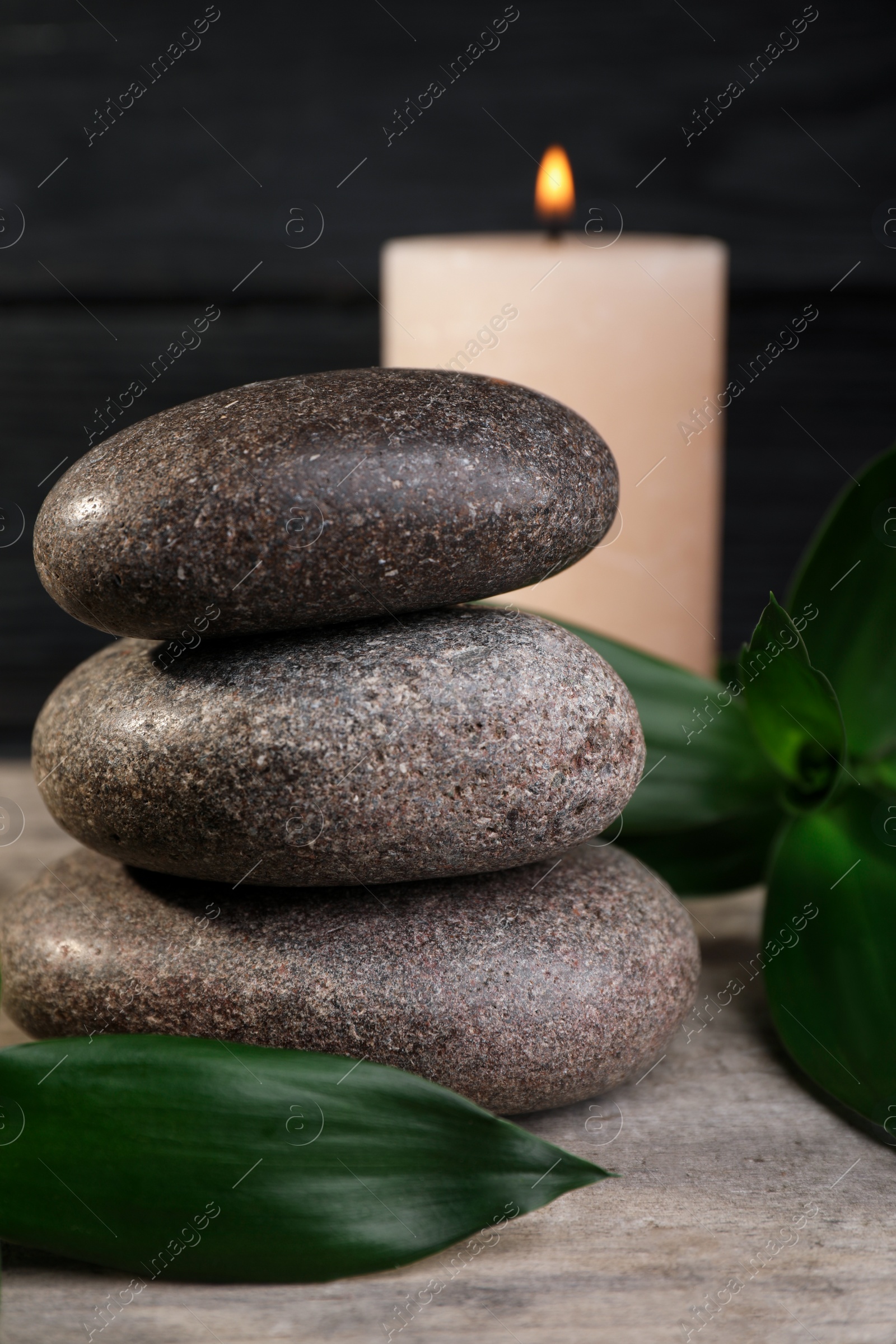 Photo of Stacked spa stones with bamboo leaves and candle on wooden table, closeup