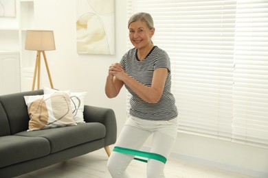 Photo of Senior woman doing squats with fitness elastic band at home