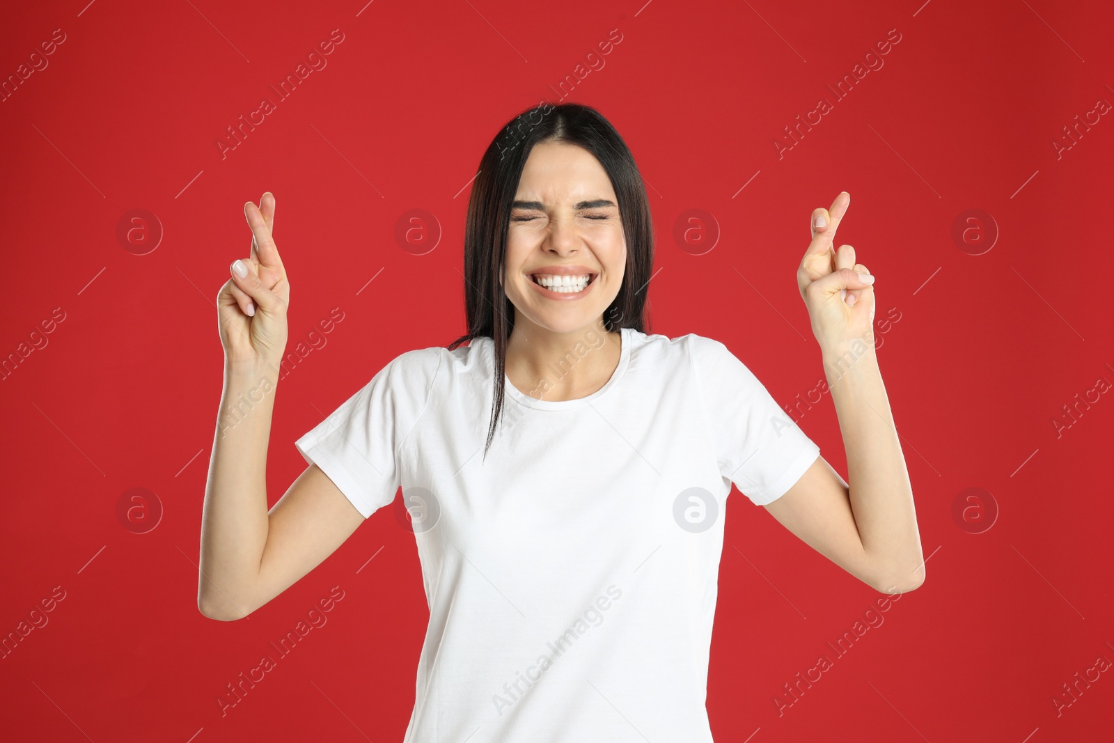 Photo of Woman with crossed fingers on red background. Superstition concept