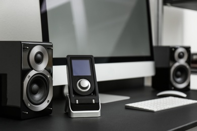 Photo of Modern computer with remote and audio speakers on table indoors