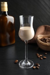 Photo of Coffee cream liqueur in glass, bottle and beans on black wooden table