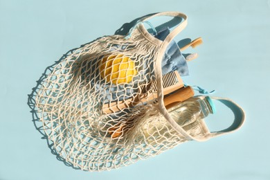 Photo of Fishnet bag with different items on light blue background, top view. Conscious consumption