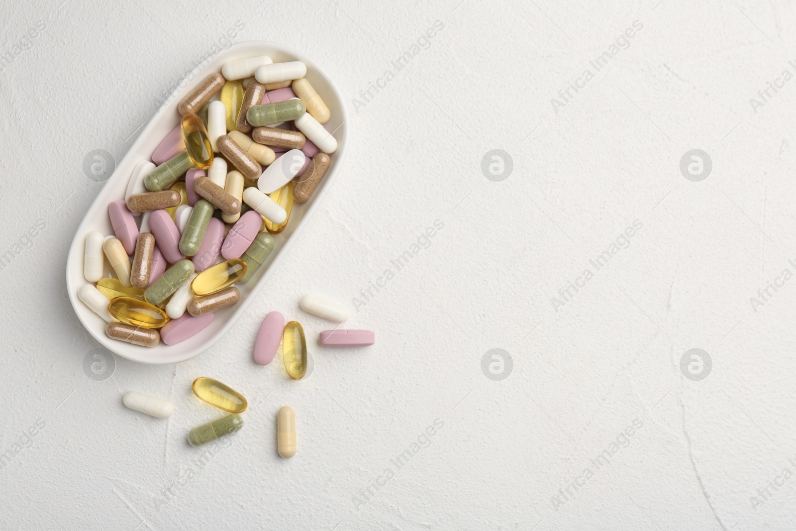 Photo of Different vitamin capsules in bowl on white wooden table, top view. Space for text