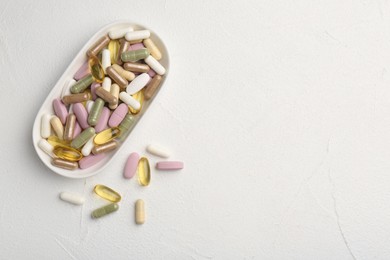 Different vitamin capsules in bowl on white wooden table, top view. Space for text