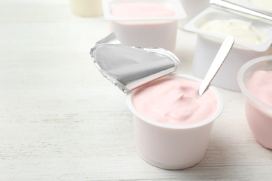 Photo of Plastic cup with fresh yogurt and spoon on white wooden table. Space for text