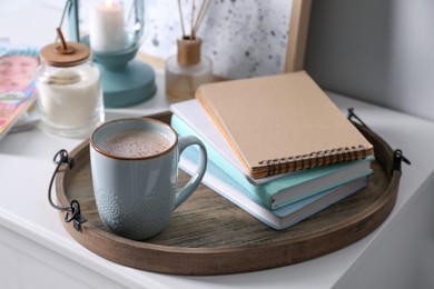 Wooden tray with books and cup of coffee on white table indoors